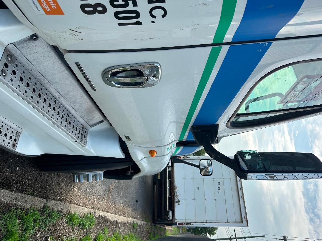 Truck cab of a 2011 Freightliner Cascadia with exterior decals, side door handle, fuel door, blue and green stripes, and side mirror visible.