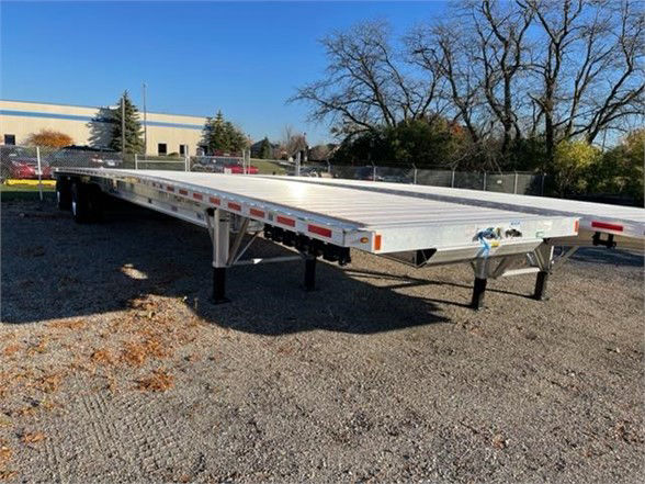 Flat aluminum Fontaine REVOLUTION 52/53ft flatbed trailer with dual axles and landing gear, showing reflective tape along sides and front coupler.
