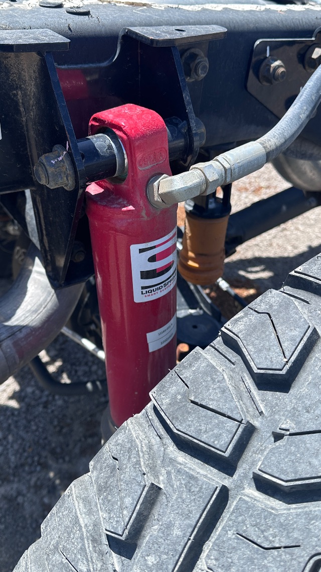 Red Liquidspring shock absorber mounted near front wheel on a Ford F-550 chassis showing hydraulic line and tire tread.