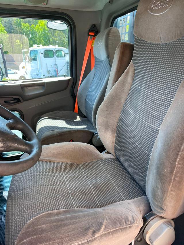 Seat interior of a 2015 Peterbilt 348 with fabric seats, steering wheel, passenger seat visible, orange seatbelt, dashboard area.