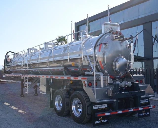 Tri-axle aluminum vacuum trailer with cylindrical tank and rear access platform, TruxTon branding, rear lights, and safety rails.