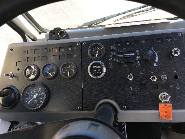 Dashboard panel of a Kalmar Ottawa YT30 yard truck showing multiple gauges, switches, gauges labeled with 'Hours' and other indicators. Navigation and ignition area with an orange tag.