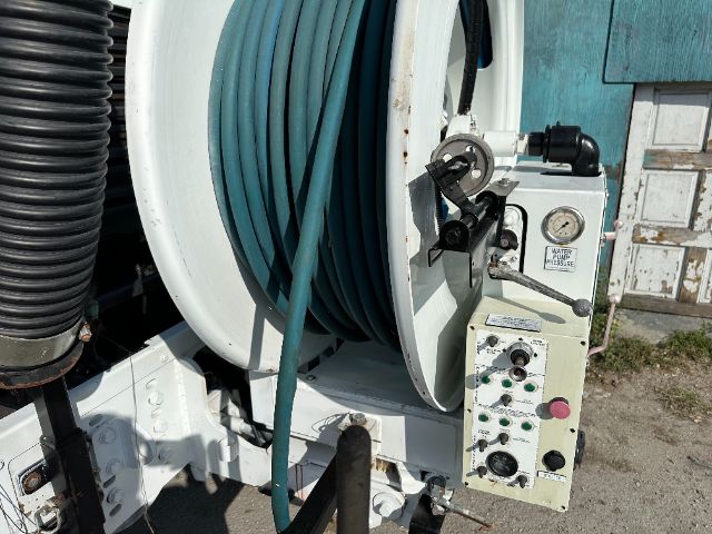 Vacuum hose reel with control panel showing gauges and valves. Coiled turquoise hose on reel. Control box with switches and gauges on right side.