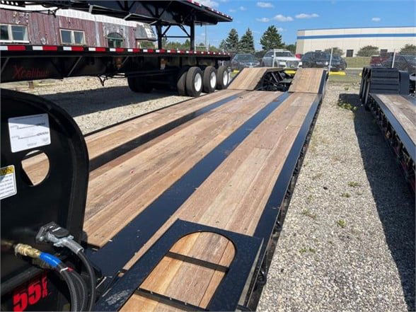 Truck trailer deck with wooden planks and lowboy configuration, showing long 24 ft steel deck and ramps; Fontaine 55 ton steel roller paver lowboy trailer in yard.