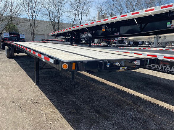 Flatbed trailer with wooden deck, black frame, red/white reflective tape along edges, with Fontaine branding visible on the frame. Low-angle view showing the long, flat surface and landing gear.