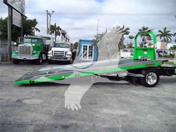 Peterbilt 536 tow truck with a long green and gray lowboy trailer in a dealership lot.