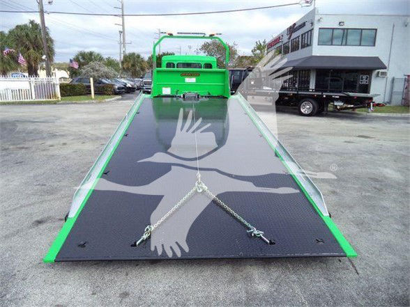 Truck bed of a 2024 Peterbilt 536 tow truck with a large black diamond-plate ramp and green frame, front cab visible in background, safety chains across ramp.