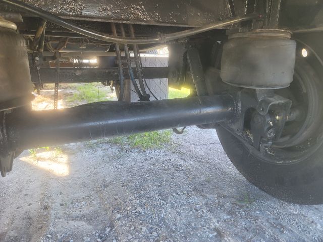 Trailer axle and leaf spring suspension with large cylindrical drive shaft and brake components visible under a flatbed trailer.