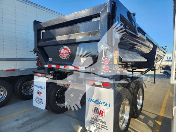 Dump trailer rear view with dual axle, black glossy dump body, rear door, reflective tape, mud flaps labeled Wabash and Ramco RR, safety stickers, and hydraulic components visible.