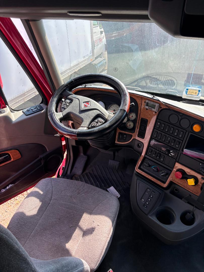 Truck cab interior showing steering wheel and dashboard of a 2016 International Prostar with woodgrain paneling and multiple control switches.