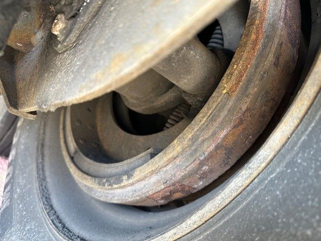 Close-up view of a 2014 Utility 4000DX trailer wheel hub and suspension components showing rusted metal and circular hub opening.