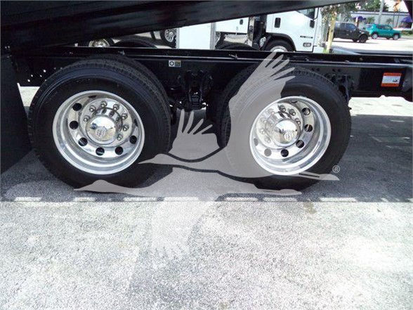 Kenworth T880 truck dual rear wheels with chrome rims and wheel covers showing undercarriage; stock photo with pavement and other trucks in background.
