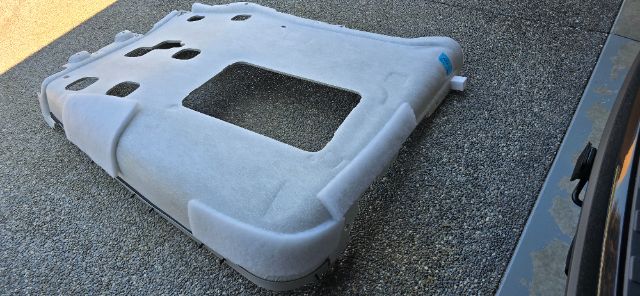 Truck seat base/frame cover with cutouts and mounting points, light gray fabric surface, blue tag visible.
