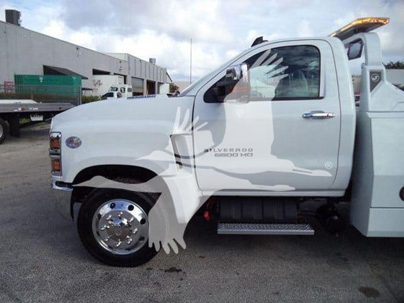 2023 Chevrolet Silverado 6500 HD side view showing cab and front wheel, with tow label on door and chrome wheel cover.
