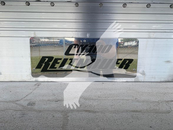 Flatbed trailer with polished metal Plaque showing Reitnouer branding and reflection of person taking photo.
