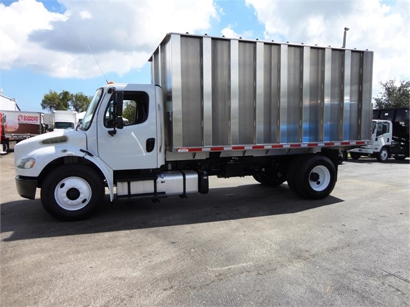 Freightliner Business Class M2 106 trash or dump body truck side view showing white cab and large metal cargo body.