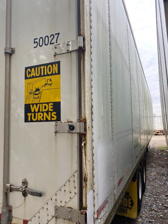Trailer rear door with caution wide turns sticker, number 50027, and hinges; side of a Wabash trailer with Duraplate exterior.