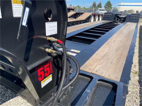Lowboy trailer deck with wooden planks and hydraulic connections on the hitch area; red '55T' label and cables attached to a black steel frame.