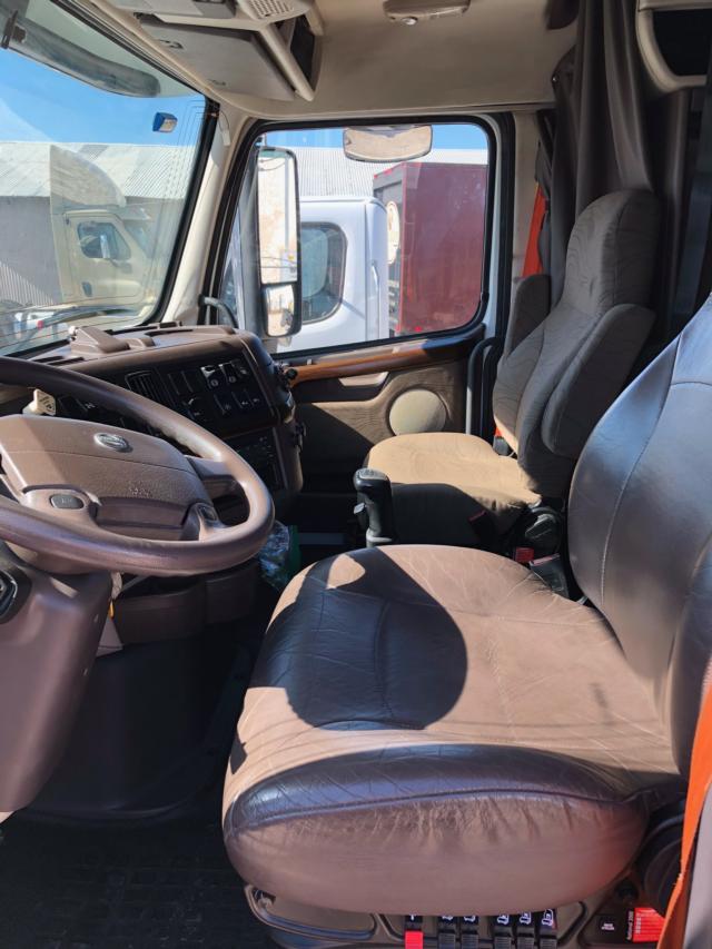 Volvo VNL64 truck cabin interior showing steering wheel, driver seat, passenger seat, dashboard, and doorway with side mirror.