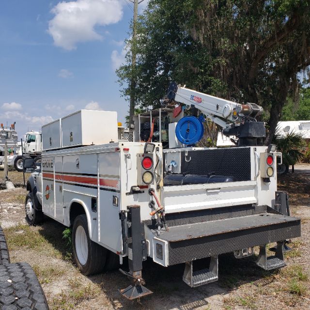 Ford F-550 utility truck rear view showing crane and service compartments with ladder rack and toolbox.