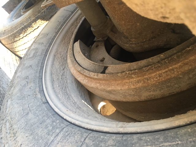 Wheel and suspension area of a trailer showing a tire with a rusty brown metal components and a large coil spring/shock, part of the axle assembly.