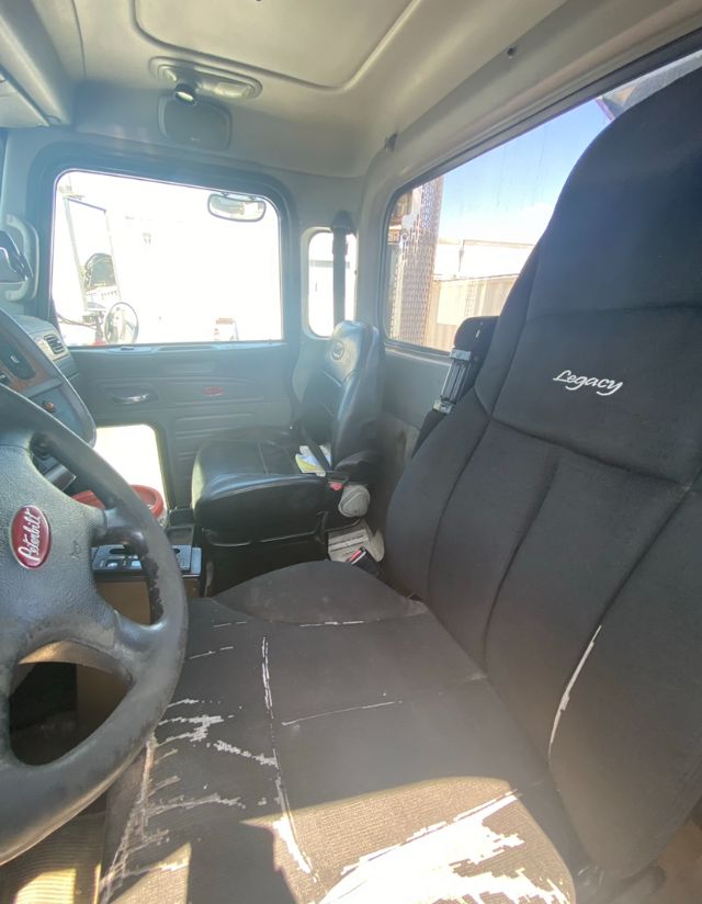 Truck interior showing driver's seat with Legacy upholstery and steering wheel, dashboard, and passenger seat. Worn seat with white scuff marks.