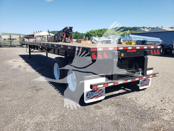 Steel flatbed trailer showing rear section with taillights, mud flaps, and reflective tape. Visible text on rear bumper plate reads ‘SED43812’ and branding plates at the back.