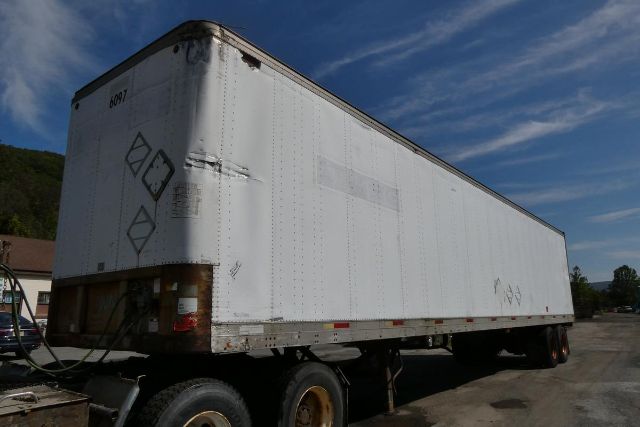 Trailer side with white exterior, Fruehauf FB9T248 trailer, dual rear axles, some rust on front edge, warning diamonds on back, VIN/stock area not visible.
