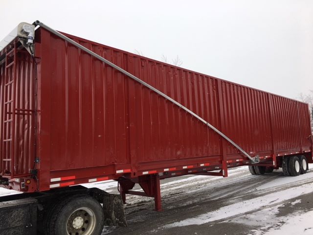 Long red scrap gondola trailer with a curved metal support along the side and dual rear axles; snow on ground.