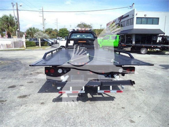 Tow truck with a flatbed trailer viewed from the rear, showing loading ramps and lighting; VIN tag visible in the background.