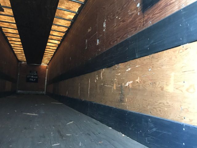 Interior of a used dry van trailer with wooden walls and a dark floor, showing sideboards and ceiling beams.