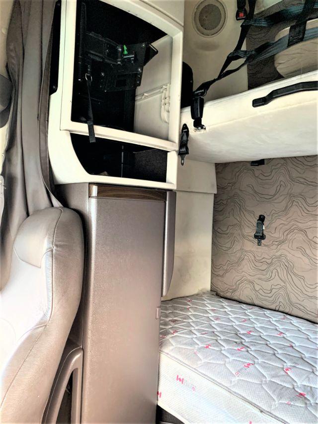 Interior of a 2015 Volvo VNL 670 truck cab showing open storage compartment and seat with sleeping area mattress.