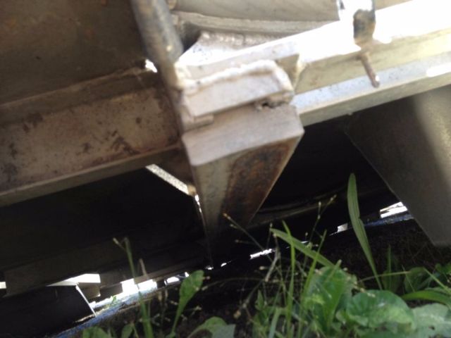 Trucks/Vacuum tank underside with rust on metal frame and green weeds nearby.