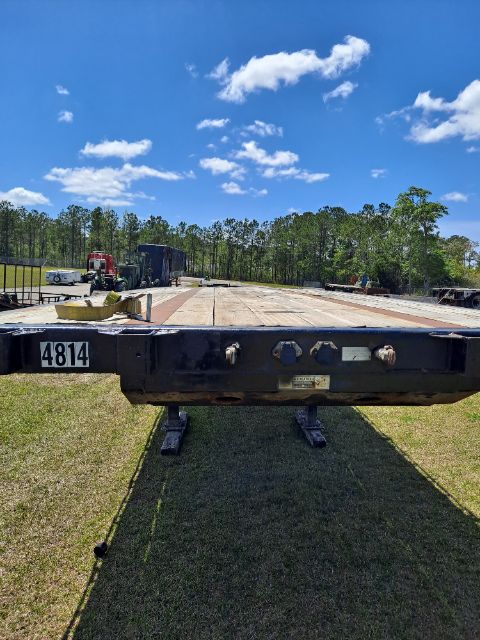 Flatbed trailer deck with control/valve panel on the side showing various fittings and a badge, VIN label visible.