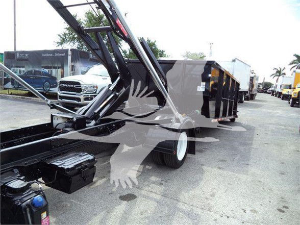 Isuzu NNR refuse truck with crane attachment and black trailer body seen in a dealership lot.