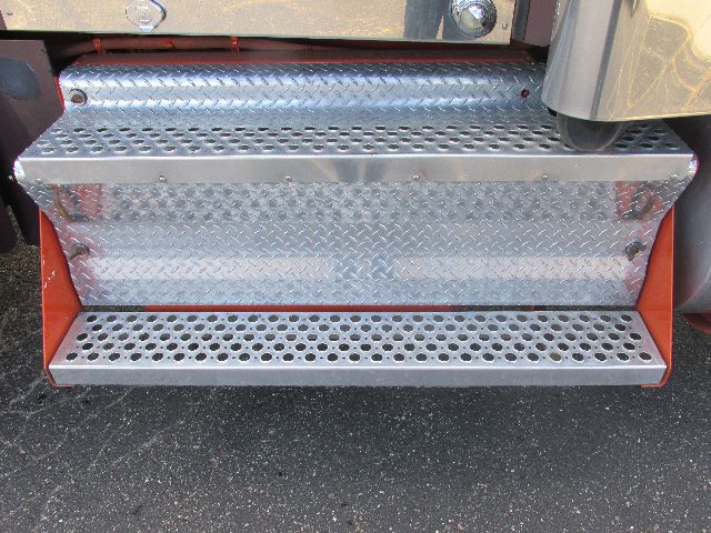 Truck steps with diamond plate metal tread and orange accents attached to a Kenworth W900 conventional sleeper, showing perforated steps.