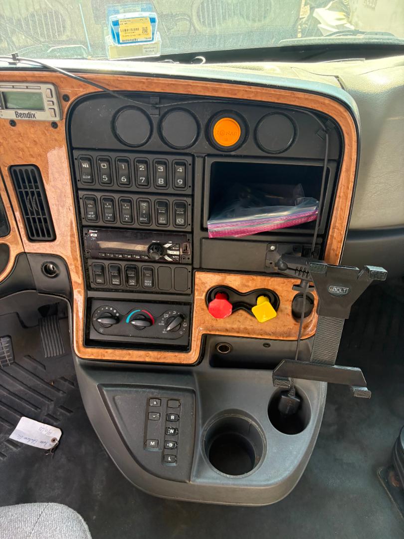 Interior dashboard of a used 2016 International Prostar showing stacked controls, wood-grain trim, instrument panel, orange push button, and cup holders.