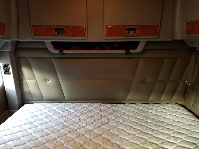 Interior of a Peterbilt 389 sleeper cab showing a quilted mattress and paneling with wood-grain accents.