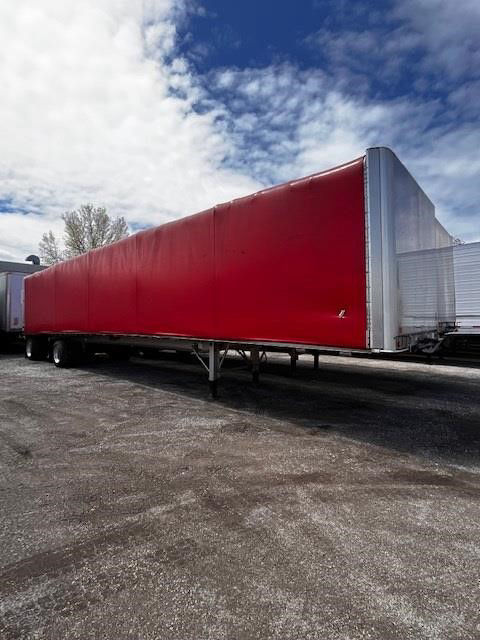 Red roll-top tarp flatbed trailer with metal frame and wheel standages, long rectangular cargo area, front gooseneck hitch not visible.