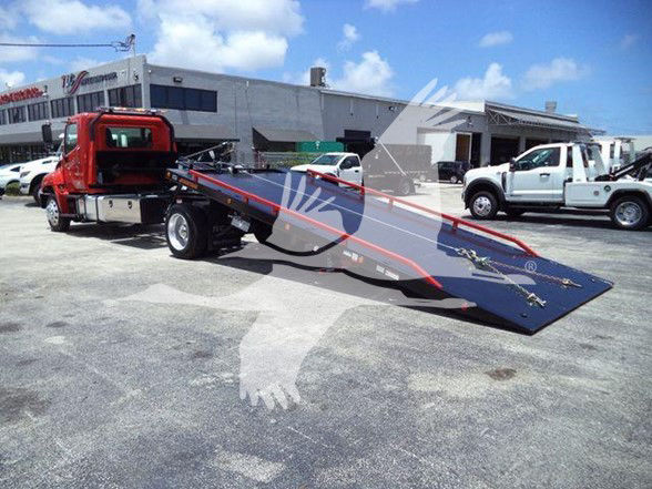 Tow truck with a red cab and a long flatbed tilt bed in a dealership lot.