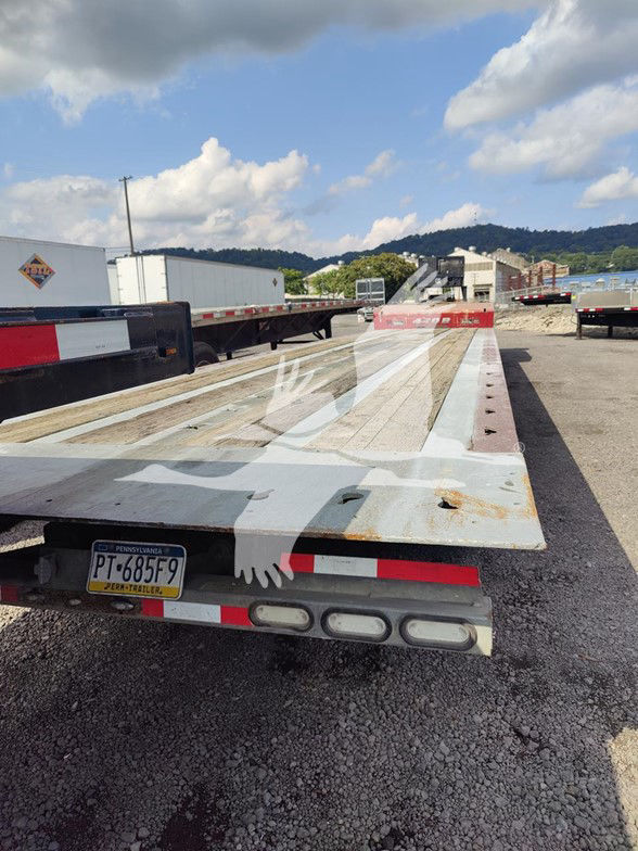 Flatbed trailer with Pennsylvania PT-685F9 license plate showing worn steel deck and rear lights.