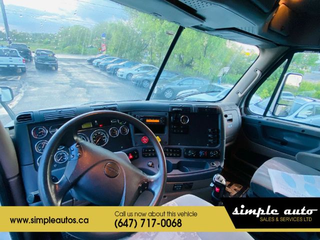 Cab interior of a Freightliner Cascadia truck showing steering wheel, dashboard gauges, and center console.