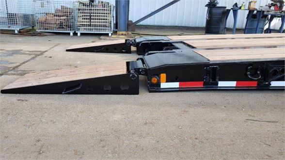 Fontaine lowboy trailer section showing long steel deck and folded ramps, black with red/white reflective stripes.