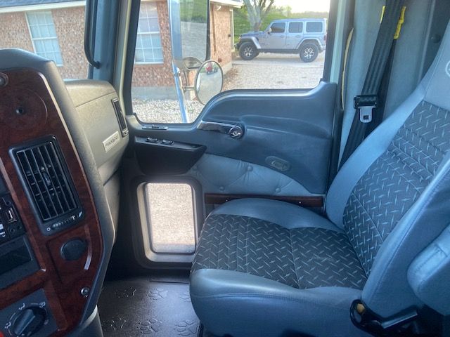 Cab interior of a 2015 Mack CXU613 truck showing driver seat, dashboard with woodgrain panel, and passenger door with window controls.