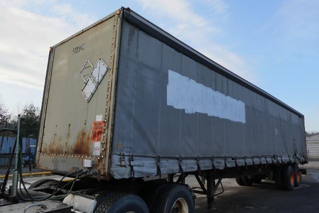 Curtainside trailer with gray tarp, rear doors, and dual rear axles in a yard.