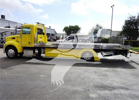 Yellow Peterbilt tow truck with flatbed, side view showing cab and long flatbed. No visible model text readable.