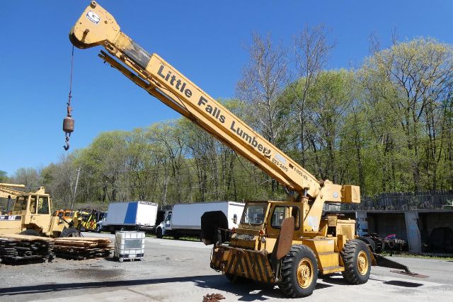 Grove RT58 mobile crane in a yard, yellow paint with black text Little Falls Lumber, long boom raised, hook block hanging, tires visible.