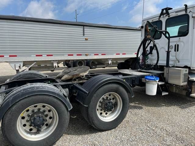 Semi truck chassis with dual rear axles and tires, Freightliner Cascadia cab in background, fuel or fluid container near cab, VIN and stock info not visible on image.