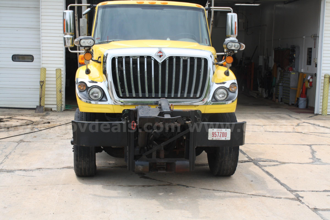 Front view of a yellow 2012 International 7400 plow truck showing chrome grille, bumper, headlights, and plow mount at the front.