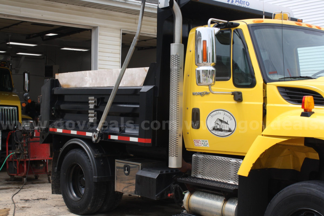 Yellow International 7400 dump truck side view showing crew cab, black dump bed, chrome exhaust stack, and emblem on door.